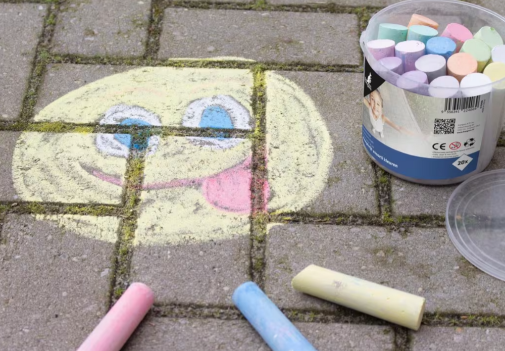 Een sfeerbeeld van Kangaro stoepkrijt op straatstenen. Er is een grote smiley getekend met geel, blauw, roze en wit krijt. Naas