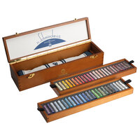 Geopende houten Schmincke pastelkist in hoekaanzicht. Beide uitneembare inlays met pastels liggen los naast de kist. In de bode