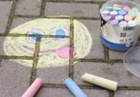 Een sfeerbeeld van Kangaro stoepkrijt op straatstenen. Er is een grote smiley getekend met geel, blauw, roze en wit krijt. Naas